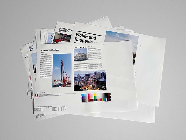 Stapel von Druckbögen und Magazinseiten auf hellgrauem Hintergrund. 