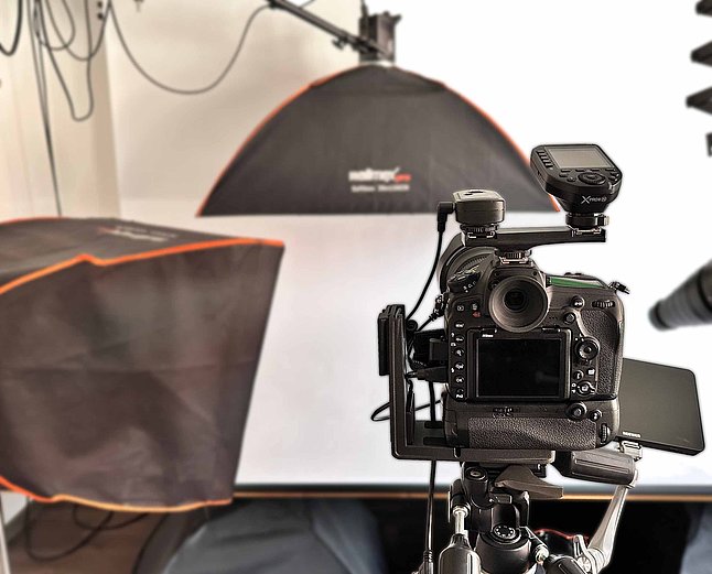 DSLR‑Kamera auf Stativ im Studio mit zwei Softboxen und weißem Hintergrund.