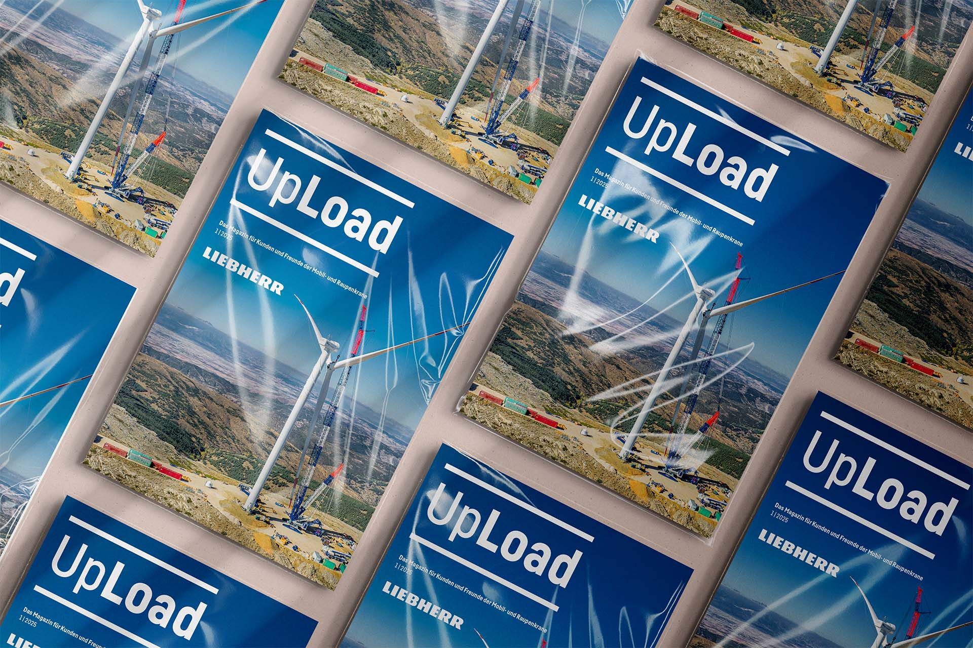 Mehrere blaue Magazine „UpLoad“ von Liebherr in Rasteranordnung, Titelbild mit Windkraftanlage. 